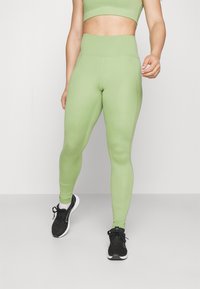 Jasnozielone legginsy z wysokim stanem, wykonane z gładkiego, elastycznego materiału. Dobierane do czarnych butów sportowych.
