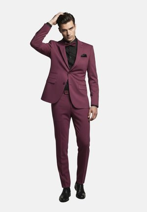 Traje ajustado color granate con camisa negra y pajarita. Presenta solapas estrechas, dos bolsillos delanteros y zapatos de vestir negros. Textura de tela suave.
