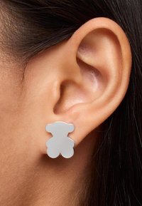 Orecchini a forma di orso grigio realizzati in materiale liscio, con una finitura lucida e bordi arrotondati, attaccati al lobo dell'orecchio.