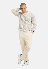 Lettere, struktureret hvid langærmet sweater med mønsterdesign og cremefarvede sweatpants. Hvide sneakers med sorte detaljer fuldender looket.