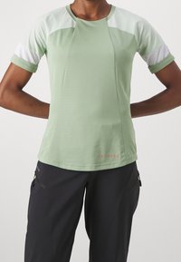 Vaaleanvihreä lyhythihainen urheilupaita, jossa on valkoisia yksityiskohtia ja teksturoitu kangas. Suunniteltu mukavuutta ja liikkuvuutta varten.