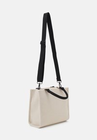 Canvas tote taske i off-white med en sort rem. Har en rektangulær form, dobbelte håndtag og en struktureret overflade. Kompakt og funktionelt design.