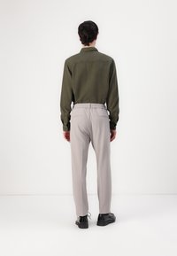 Camisa verde de manga larga con puños abotonados combinada con pantalones gris claro que tienen una cintura elástica. Zapatos negros completan el conjunto.
