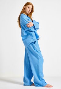 Modrý dvojdielny loungewear set vyrobený z textúrovaného materiálu. Vrchná časť má voľný strih s dlhými rukávmi a nohavice sú široké a voľné.