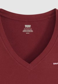 Burgunderfarget bomull V-hals t-skjorte med en glatt tekstur, med et lite rødt Levi's-logo nær kanten og vaskeanvisning ved halsen.