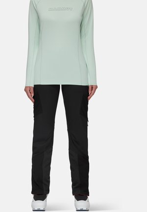 Mint green long-sleeve top with MAMMUT logo; paired with black pants featuring textured panels and zippers; worn with white boots.