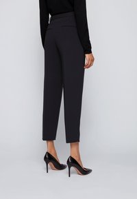 Musta räätälöity housut, joissa on slim fit -leikkaus, lyhyt pituus, litteä etuosa ja takataskut, yhdistettynä mustiin korkeakorkoisiin kenkiin.