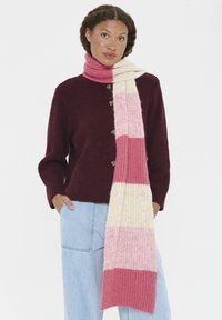 Écharpe en tricot avec des rayures roses, des sections crème et rose clair. Texture douce, accompagnée d'un pull bordeaux avec des boutons et d'un jean bleu clair.