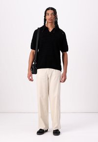 Tricou polo tricotat negru cu mâneci scurte, asortat cu pantaloni largi de culoare crem și pantofi slip-on negri. Geantă minimalistă tip crossbody.