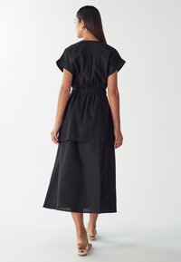 Abito lungo nero con vita cinchata, maniche corte e design a strati per un pizzico di texture. Semplice, elegante e realizzato in tessuto leggero.