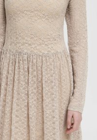 Spitzenkleid in hellem Beige, mit langen Ärmeln und einem gerafften Rock. Filigranes Blumenmuster und strukturierte Oberfläche über das gesamte Kleid.