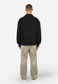 Μαύρο πλεκτό μπουφάν με άνετη εφαρμογή και χαμηλούς ώμους, συνδυασμένο με ανοιχτό γκρι βελούδινα παντελόνια που διαθέτουν μπροστινές τσέπες.