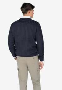 Granatowy sweter w splot warkoczowy z wysokim kołnierzem, długimi rękawami i ściągaczami, zestawiony z beżowymi spodniami cargo z bocznymi kieszeniami.