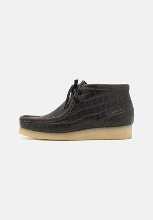 Black leather boot with crocodile texture, round toe, lace-up front, and a soft beige rubber sole. Classic design with minimal accents.