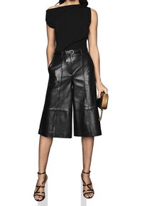 Czarne skórzane kuloty o wysokim stanie, z przeszyciem i szerokimi nogawkami. Zestawione z czarnym topem bezrami i sandałami na obcasie.