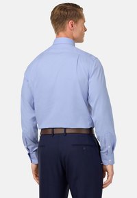 Camicia a quadri azzurri chiari con maniche lunghe, polsini a bottoni e colletto strutturato, abbinata a pantaloni blu scuro e una cintura marrone.