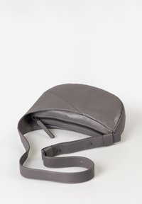 Ronde grijze leren tas met een ritssluiting en een lange, verstelbare schouderband. Gladde textuur met een subtiele stikaccent langs de randen.