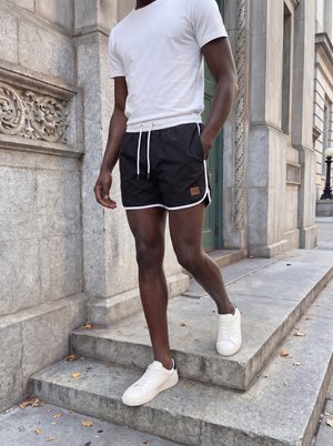 Man wearing white t-shirt, black shorts, and white sneakers walking down stone steps beside ornate building.