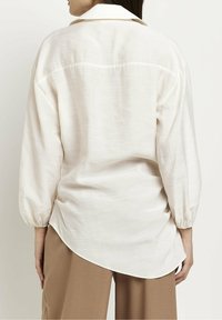 Lightweight, cream blouse with long, gathered sleeves and a button-down collar. Curved hem and subtle textured fabric detail.
