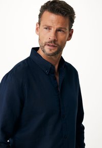 Camicia button-up blu navy realizzata in un tessuto leggero, con colletto a punta e una sottile trama, dotata di chiusura con bottoni tradizionale.