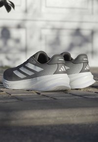 Graue Sportschuhe mit drei weißen Streifen, Mesh-Obermaterial, gepolstertem Schaft und einer weißen Zwischensohle. Strukturiertgummi-Außensohle für besseren Halt.