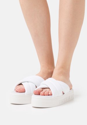 Sandales plateformes blanches avec des brides en tissu croisées et une semelle texturée. La marque "TOMMY JEANS" est estampillée sur le côté.