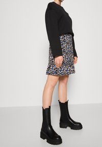 Sweatshirt nero corto abbinato a una mini gonna a fiori nei toni del blu e beige. Stivali alla caviglia neri e chunky con pannelli elastici laterali.