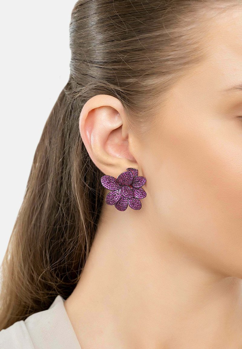 Pendientes en forma de flores moradas con una superficie texturizada adornada con acentos brillantes, presentando múltiples diseños de pétalos y un cierre tipo botón.