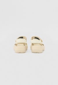 Beige sandaler med justerbare stropper, gummisåle og strukturert overdel. Har en bakre hælreim for sikker passform. Minimalistisk design.