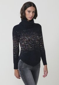 Pleten pulover s turtleneck ovratnikom v temno modri barvi z barvnim mešanim vzorcem. Ima dolge rokave in ukrivljen rob za prilegnjeno silhueto.