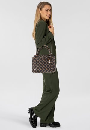 Borsa nera con dettagli dorati a motivo, design strutturato e due manici, indossata con un completo verde. Scarpe nere lucide completano il look.