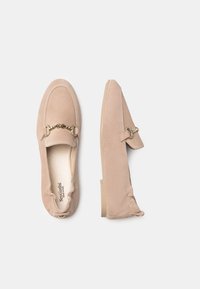 Beige suède loafers met een gouden kettingaccent, ronde neus, flexibele zool en gestikte details langs de randen.