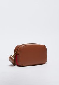 Trousse de maquillage rectangulaire en cuir marron avec une fermeture éclair dorée, un accent rayé rouge et une poignée détachable. Texture lisse, design minimaliste.