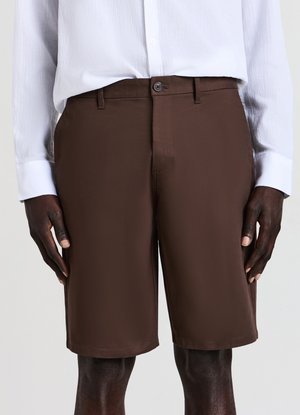 Brown shorts with a smooth texture, tailored cut, and a single button closure. Paired with a lightweight white long-sleeve shirt.