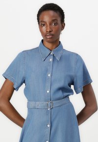 Denim shirt dress with short sleeves, collar, front button closure, and a belted waist. Light blue color and subtle stitching detail.