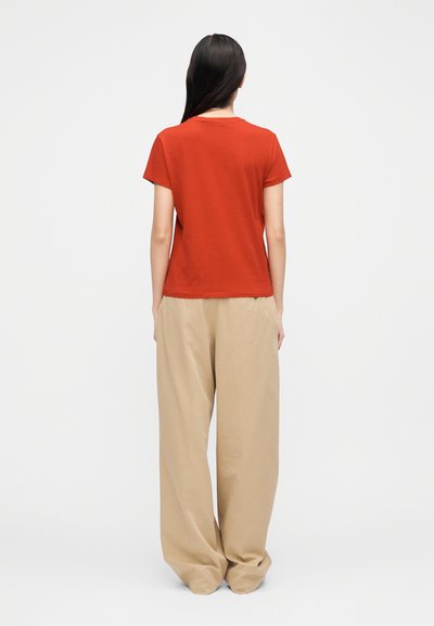 Piros pamut póló kerek nyakkivágással, laza szabású bézs nadrággal, mely laza kialakítást és sima textúrát tükröz.