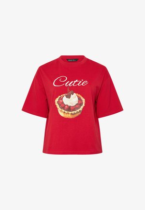 Camiseta roja de manga corta con texto "Cutie" y un gráfico de tarta de cereza cubierta con crema batida en el frente.