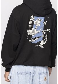 Svart hoodie med en grafisk design på baksidan med vita körsbärsblommor och koi-fiskar mot en blå bakgrund. Mjuk textur.