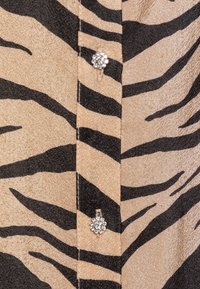 Tan shirt with black tiger stripes, featuring sparkling floral buttons along the placket. Material has a subtle sheen and smooth texture.