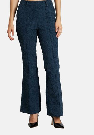Pantalones acampanados azul marino con un patrón floral texturizado, que cuentan con una cinturilla alta y detalles en las costuras laterales. Combinados con tacones altos negros.