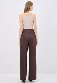 Bruine high-waisted wijde broek van textuurstof, gecombineerd met een ribbelbeige top met een gouden kettingdetail op de schouderbanden.