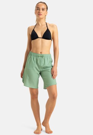 Hellgrüne Badeshorts mit elastischem Bund und Kordelzug, kombiniert mit einem schwarzen dreieckigen Bikini-Oberteil. Glattes Material, lässige Passform.