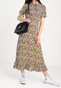 Abito midi floreale con collo rotondo, maniche corte, orlo a volant e stampa multicolore; abbinato a una borsa nera e sneakers bianche.