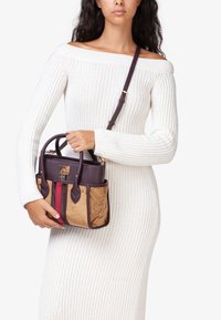 Borsa strutturata in pelle viola con base in suede beige, accentuata da strisce rosse e motivi floreali in rilievo.