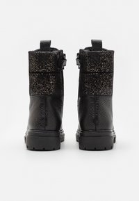 Černé kotníkové boty s texturovanou kůží, lesklou černou částí a třpytivým svrškem. Mají zesílený podpatek a poutko.