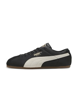 Sneaker Puma nero a profilo basso con striscia laterale beige, lacci neri e suola color gomma, vista della parte esterna sinistra con marchio "Puma Tackle".