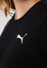 Primo piano di una persona che indossa una maglietta sportiva nera con un piccolo logo bianco Puma sul petto.