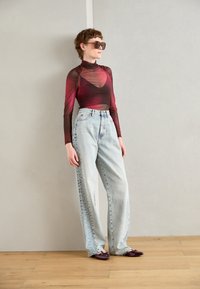 Haut à manches longues transparent en dégradé rouge à marron, associé à un jean baggy taille haute bleu clair. Chaussures à bout pointu de couleur violet foncé.