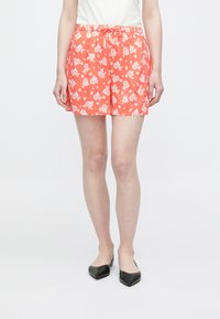 Röda shorts med blommönster och vita blommor, elastisk midja och dragsko. Tillverkade av lätt tyg med lös passform.