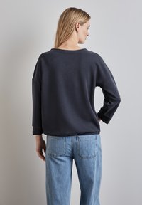 Tmavě šedá oversized mikina s širokým výstřihem, dlouhými rukávy a hladkým povrchem, oblečená s světle modrými džíny s vysokým pasem.